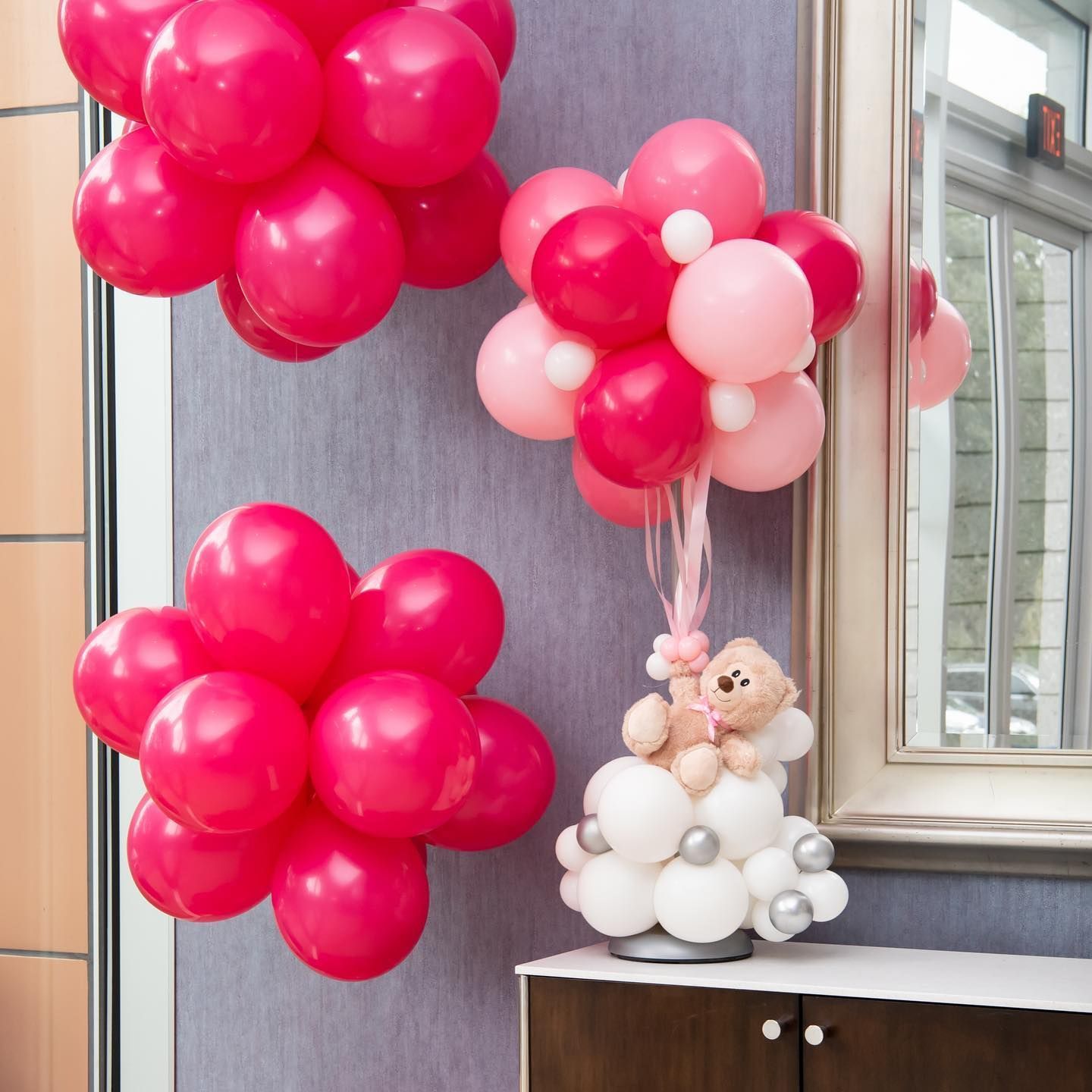 A teddy bear is sitting on a cloud made of balloons for a baby shower