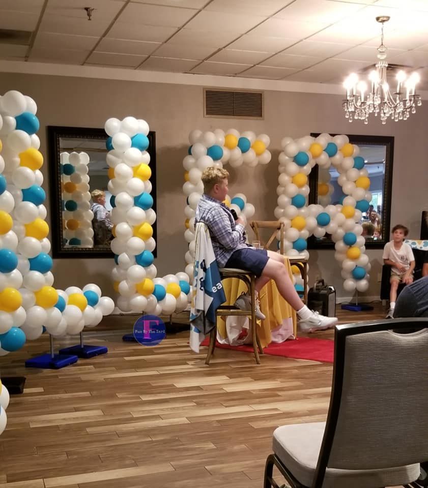 A man sits in a chair in front of balloons that spell out BALLER