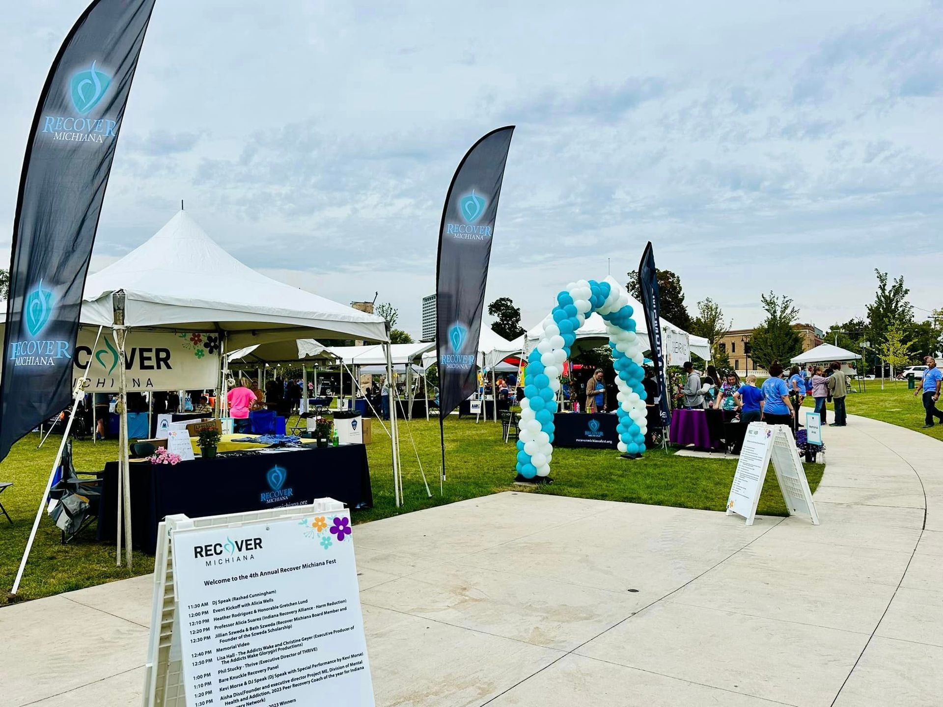A group of people are gathered in a park with tents and balloons.