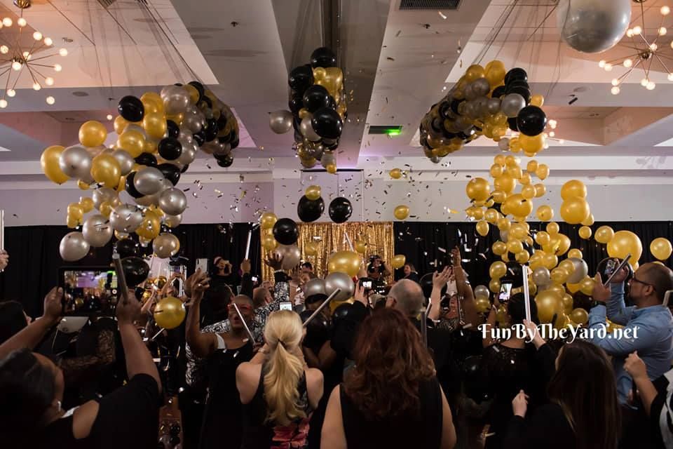 A crowd of people are gathered in a room with balloons and confetti. Balloon Drop