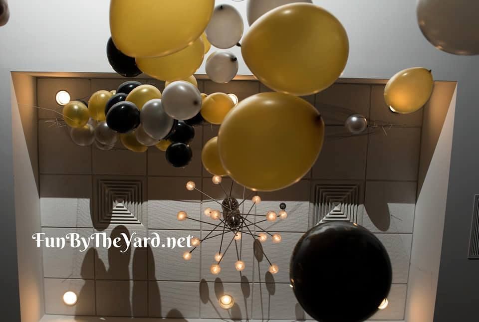 A bunch of yellow and black balloons hanging from the ceiling. Balloon drop