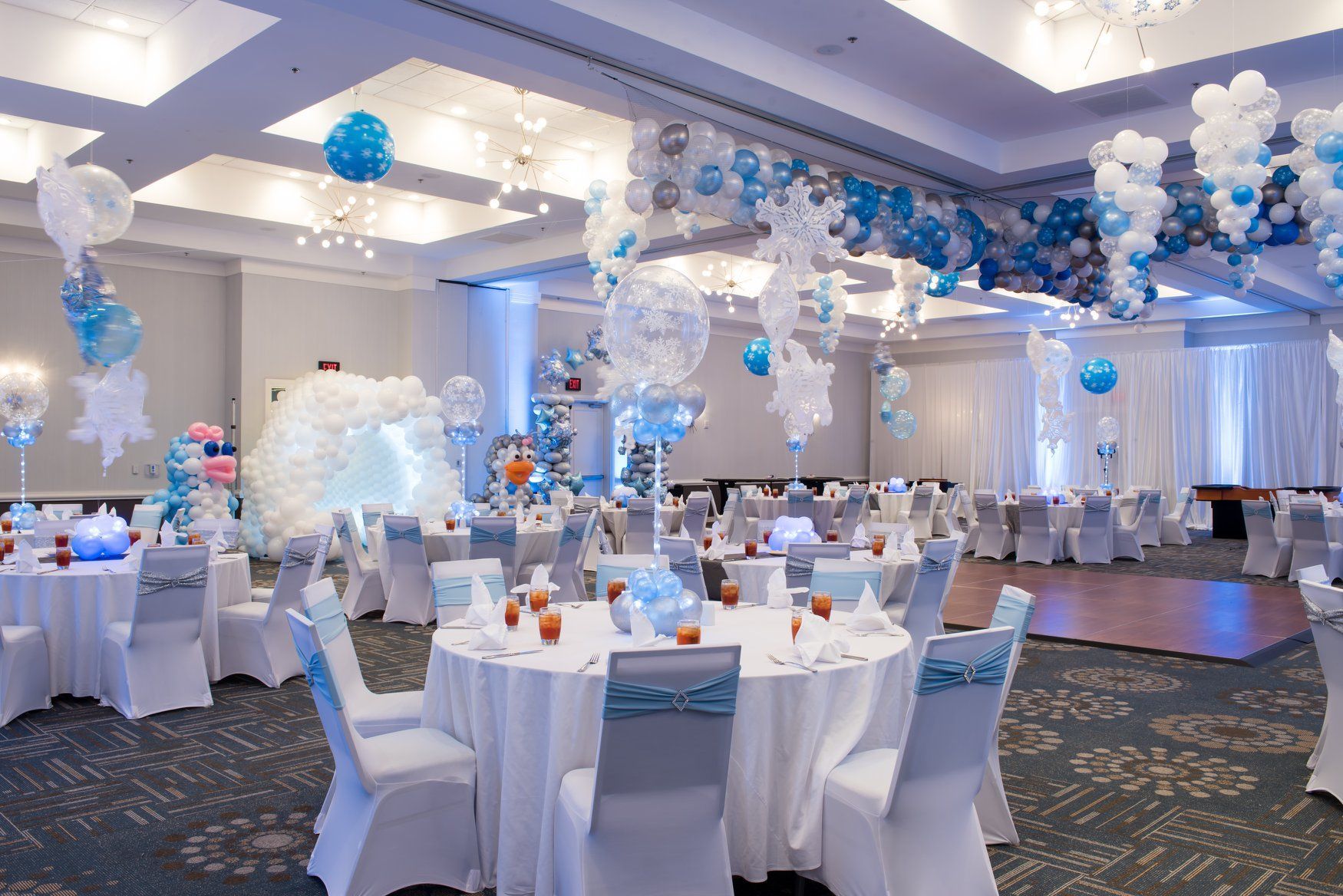 A large room filled with tables and chairs and balloons. Christmas winter wonderland themed party