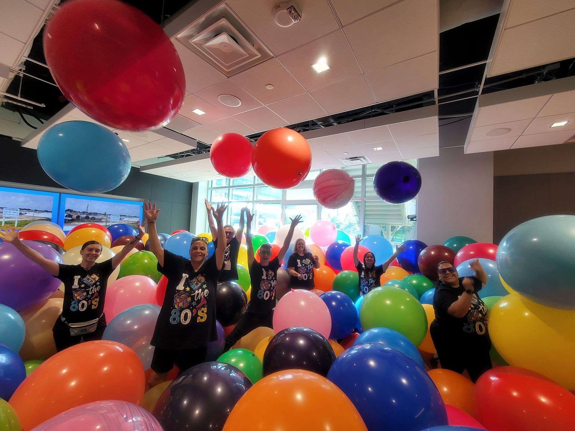 A group of people are standing in a room filled with balloons. Party Bomb