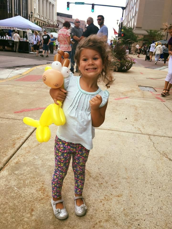 A little girl is holding a balloon giraffe on a sidewalk.