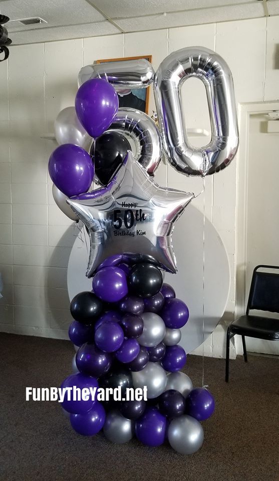 A bunch of purple , black , and silver balloons on a pole.
