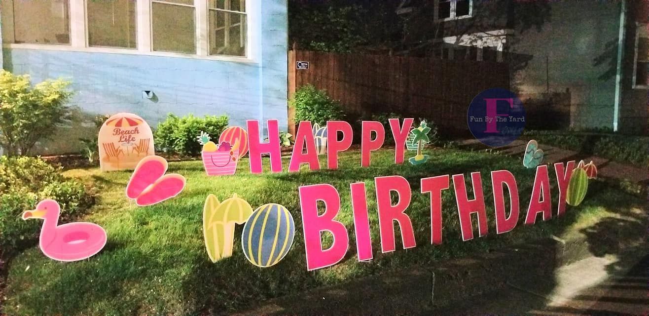 A happy birthday sign is sitting in the grass in front of a house. Beach themed yard card.