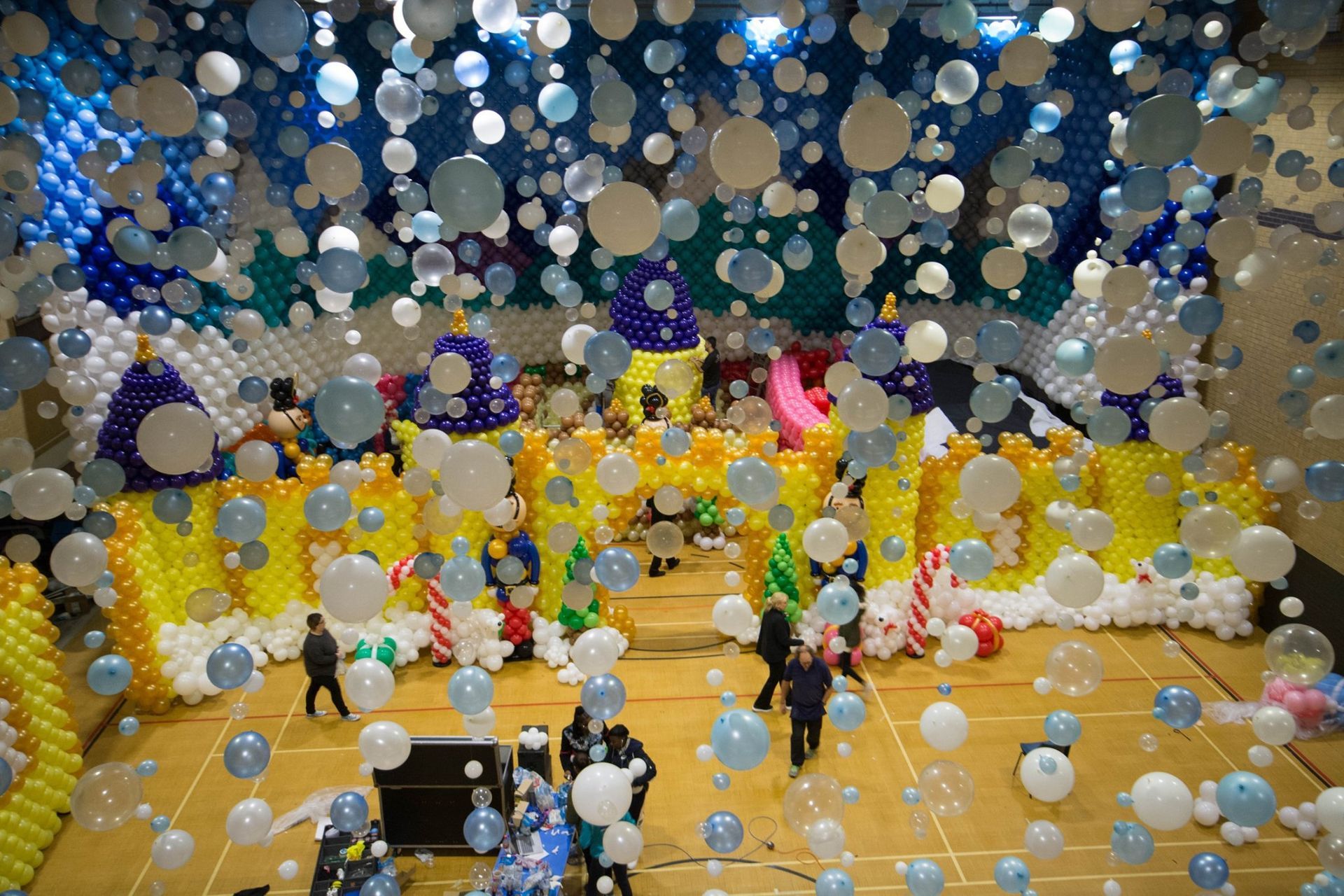A bunch of balloons are hanging from the ceiling of a gym.