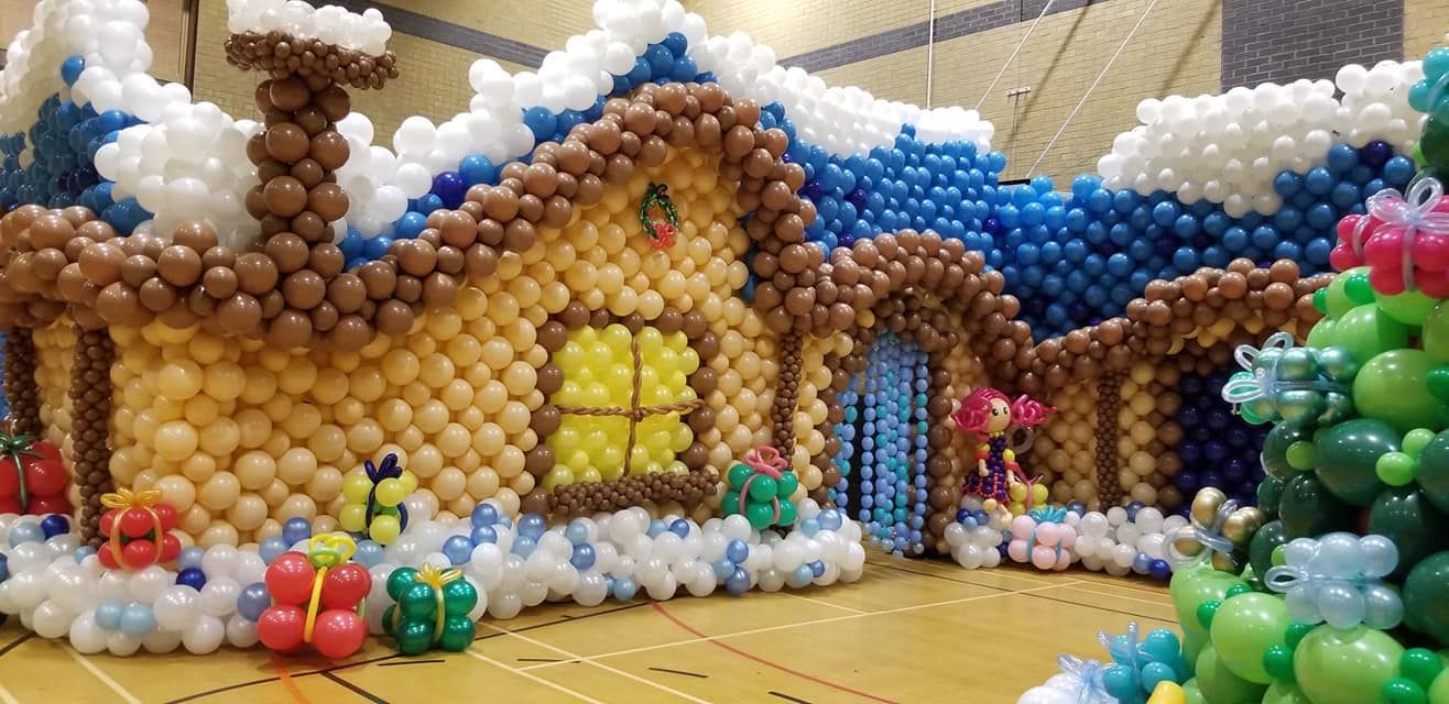 A house made out of balloons with a christmas tree in front of it.