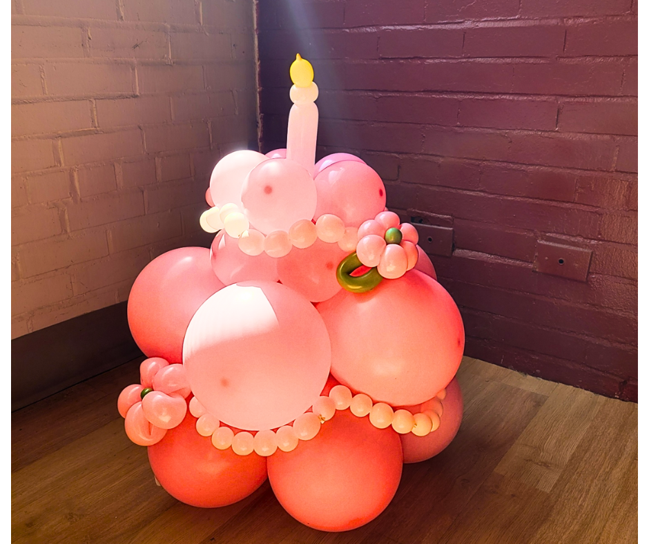 Pink balloon cake with a balloon candle on a wooden floor.