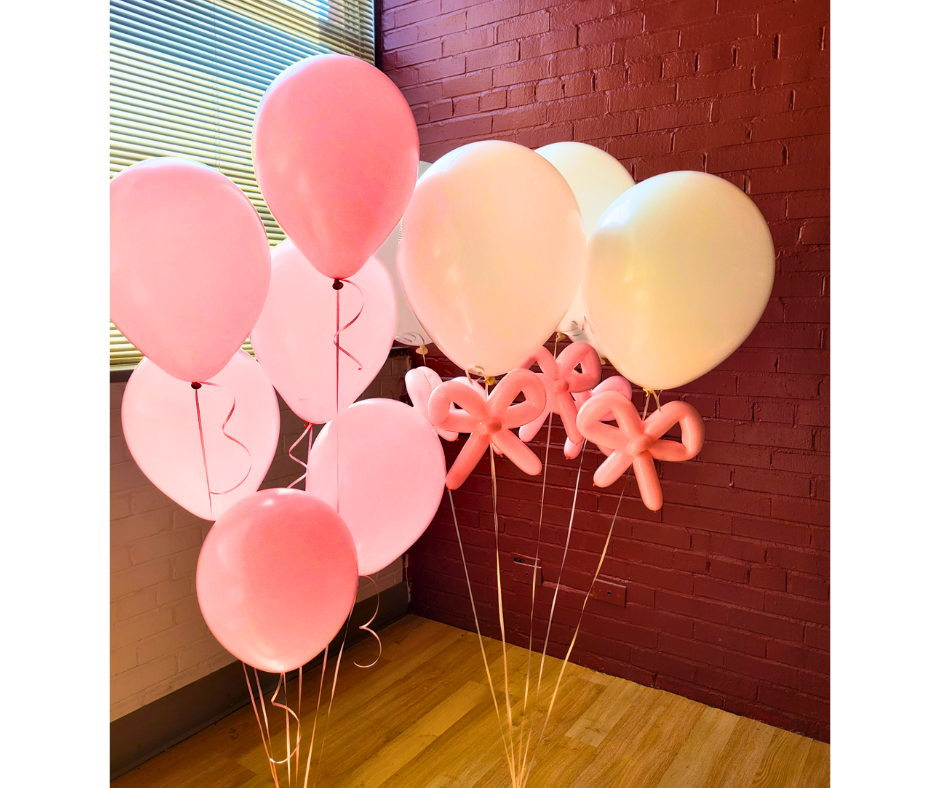 A bunch of pink and white balloons against a brick wall with pink ribbons