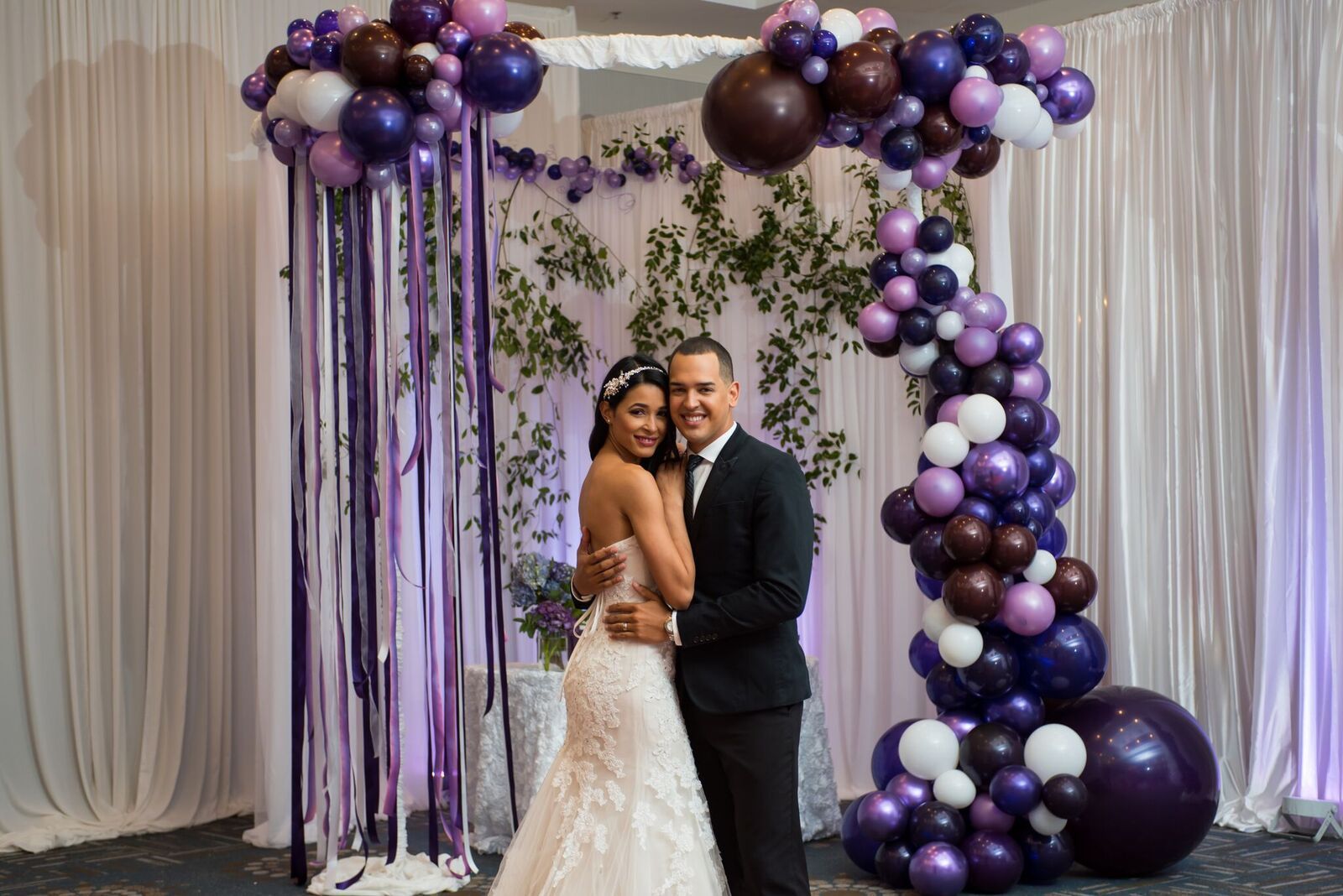 A bride and groom are posing for a picture in front of a balloon garland