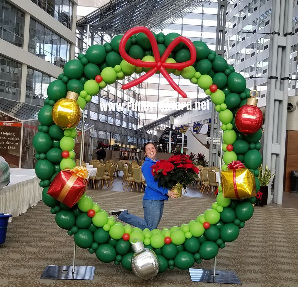 A woman stands in front of a christmas wreath made of balloons