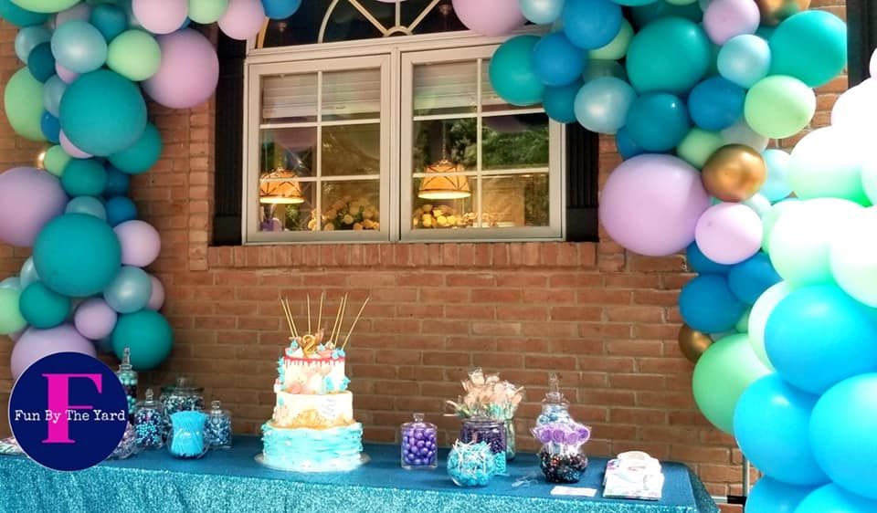 A table with balloons and a cake on it in front of a window.