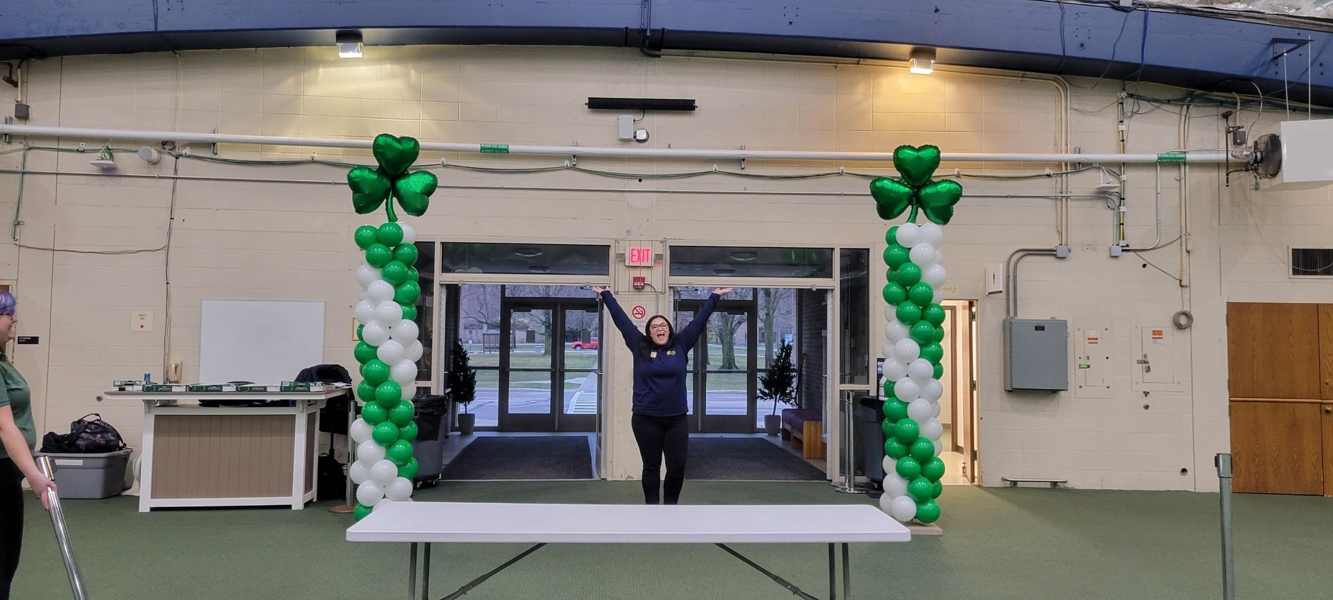 A man is standing in front of a table decorated with green and white balloons.