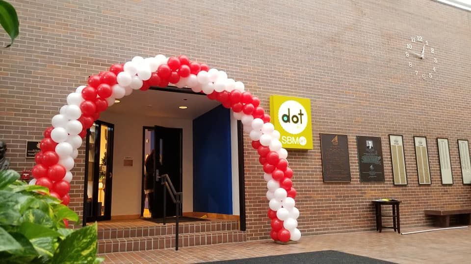 A red and white balloon arch is in front of a building that says dat