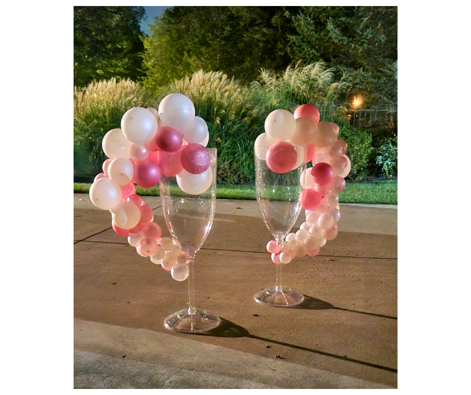 Two large champagne glasses decorated with pink and white balloons on a sidewalk.