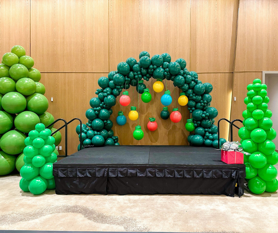 A stage decorated with green balloons in a Christmas theme. Green arch, trees, and ornaments.