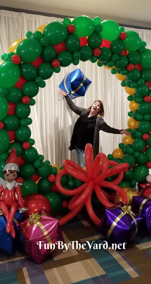 A woman is standing in front of a christmas wreath made of balloons.