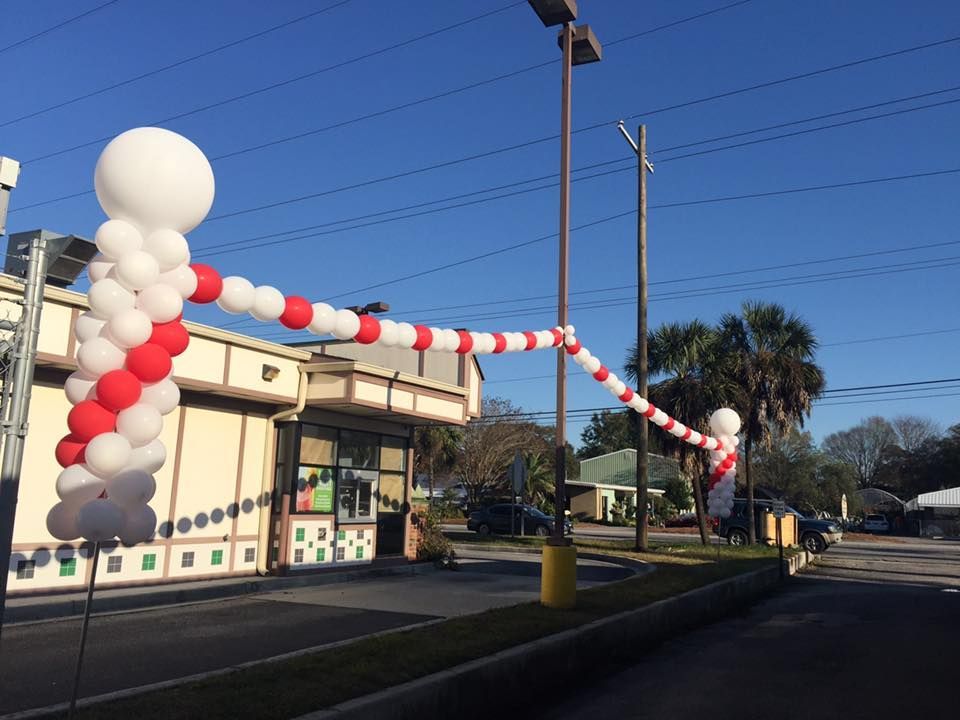Drive-through restaurant with red and white balloon archway decoration. Bright, sunny day.