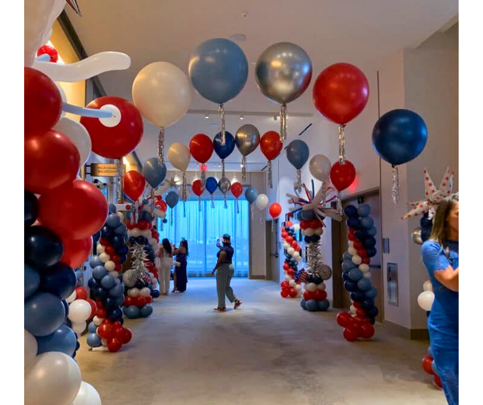 Hallway decorated with red, white, and blue balloons. People are present.