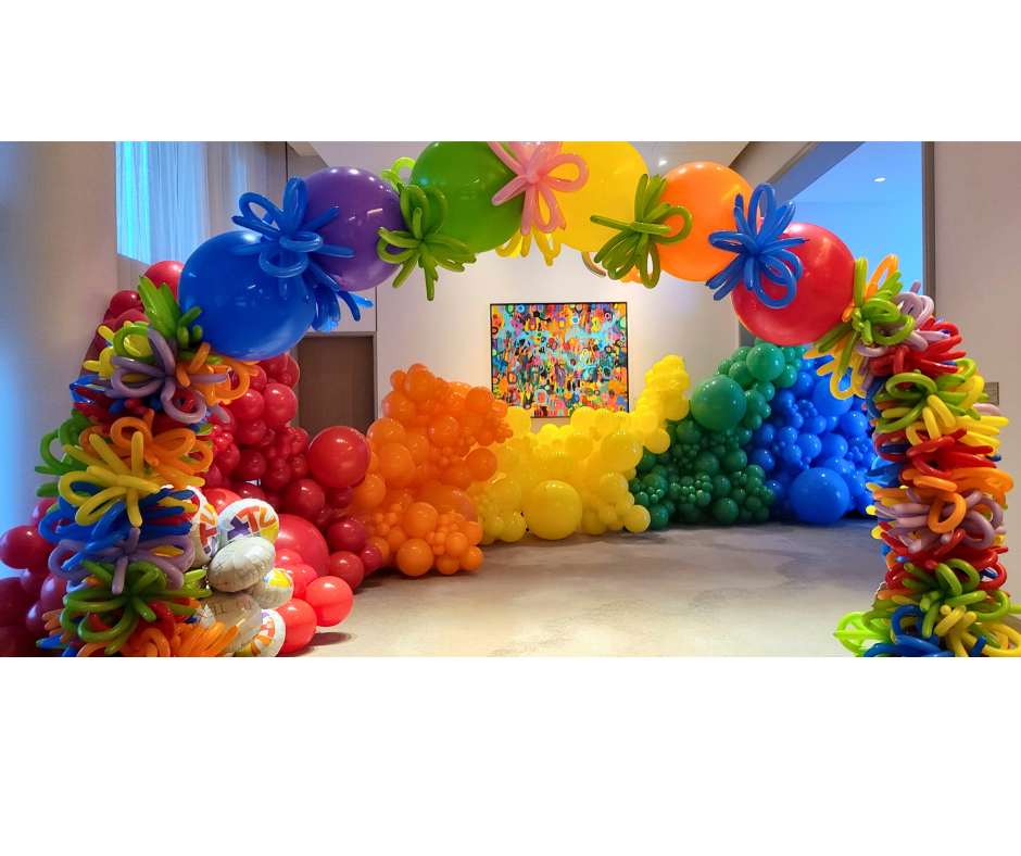 Colorful balloon archway with various rainbow-colored balloons. The setting appears to be an event or party.