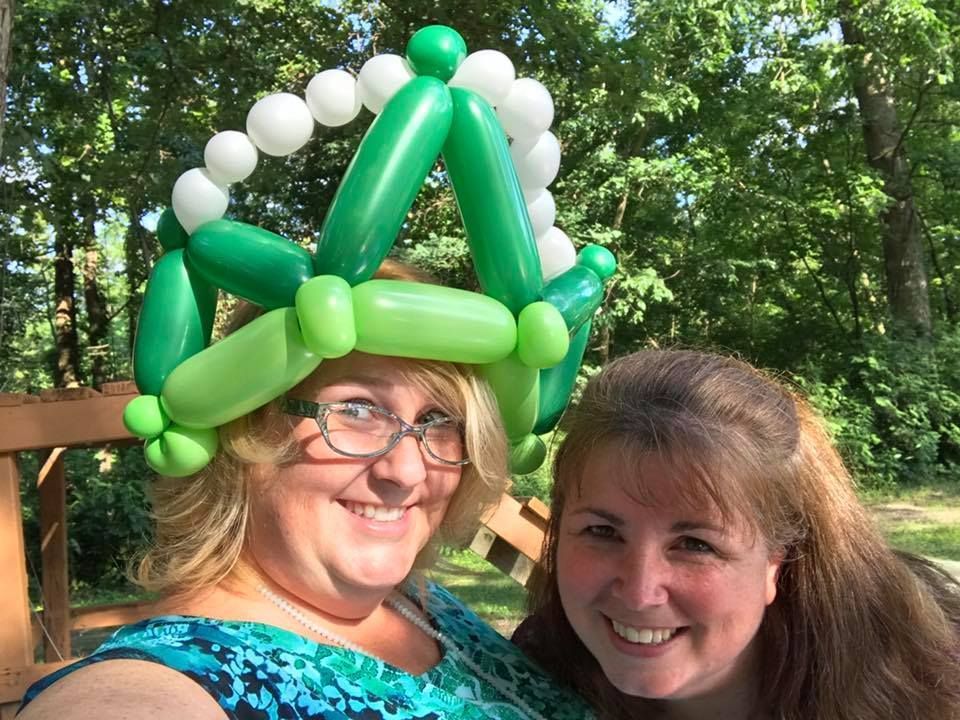 Two women are posing for a picture with one wearing a green balloon hat.