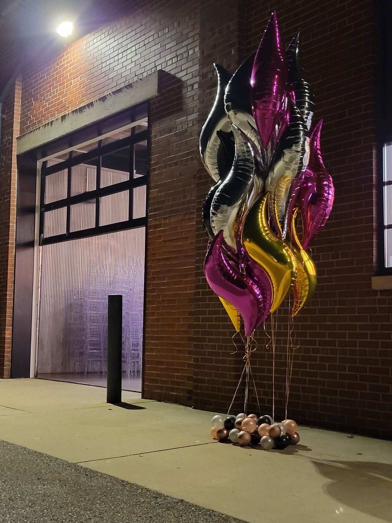 Balloons in various colors tied to weights in front of a brick building with a garage door.