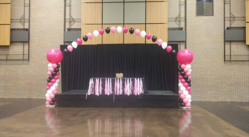 A stage decorated with pink , white and black balloons in a room at Century Center.