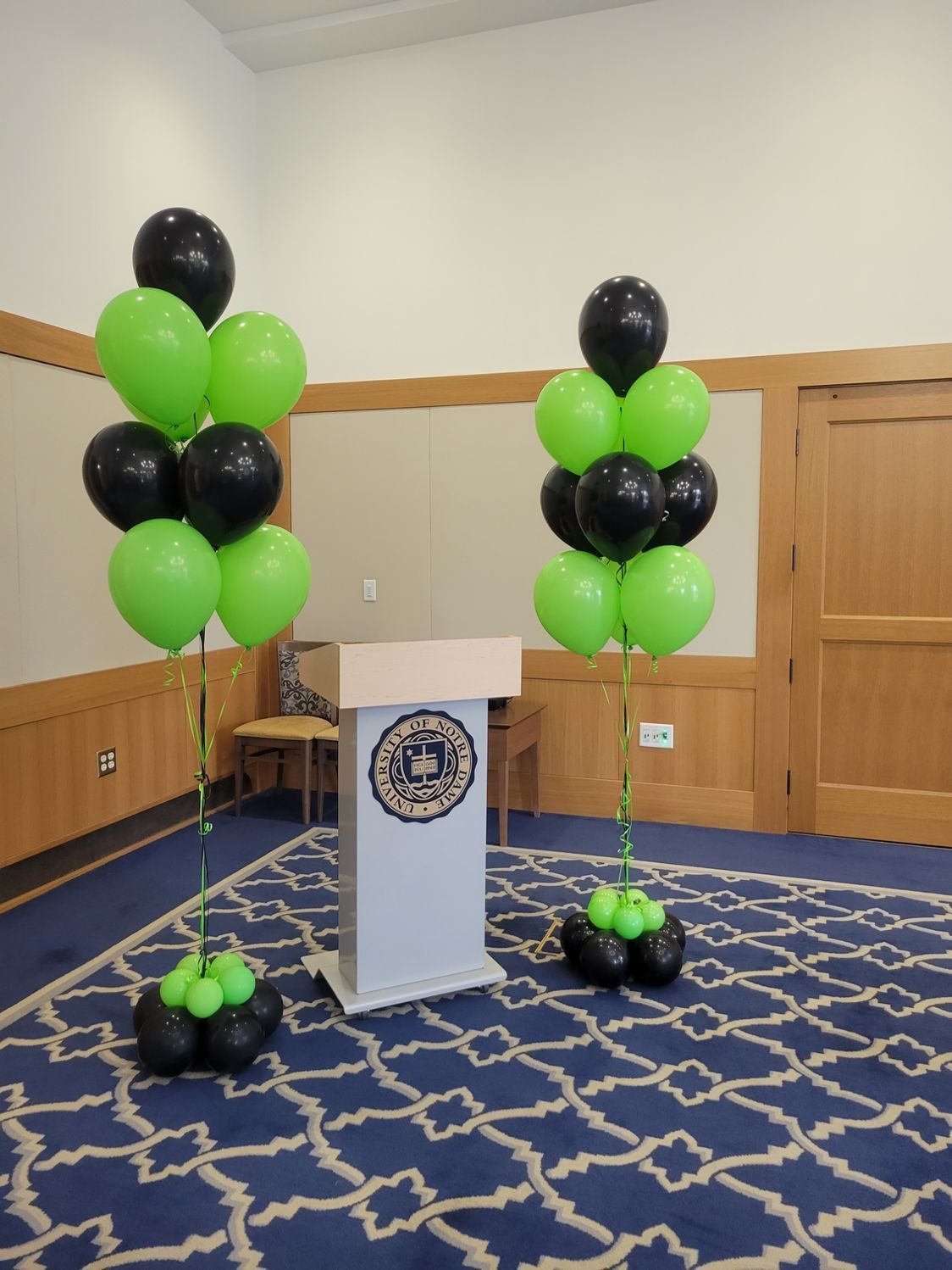 Two green and black balloon columns flanking a podium on a blue patterned carpet.