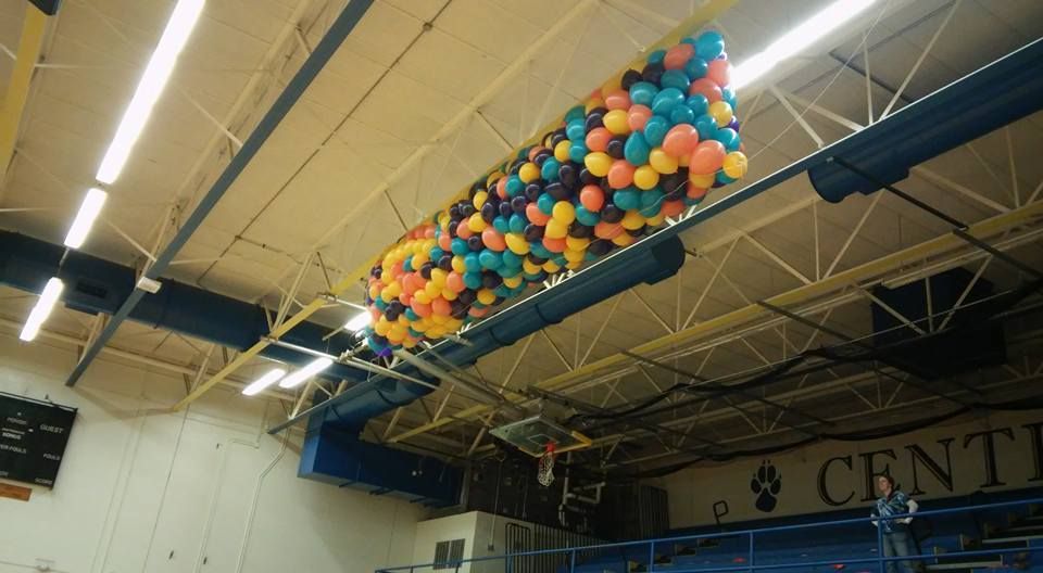 A bunch of balloons are hanging from the ceiling of a gym.  Balloon Drop