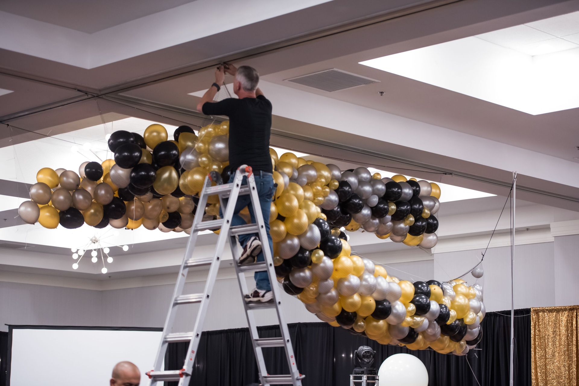 A man is standing on a ladder decorating balloons in a room.