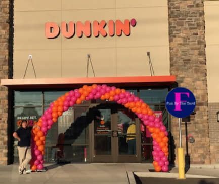 A dunkin ' donuts store with a pink and orange balloon arch