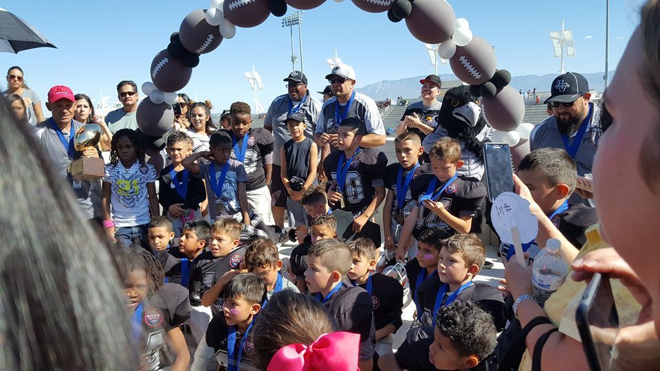 A group of children are standing under an arch of balloons.