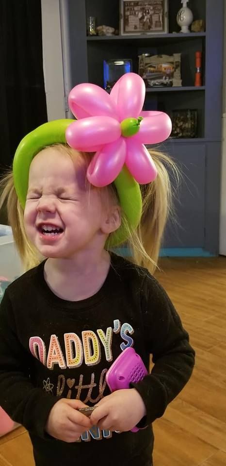 A little girl is wearing a flower made of balloons in her hair.
