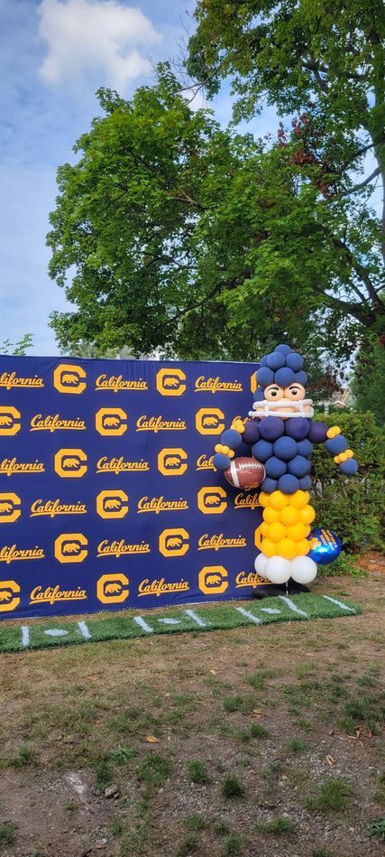 A football player made out of balloons is standing in front of a sign.