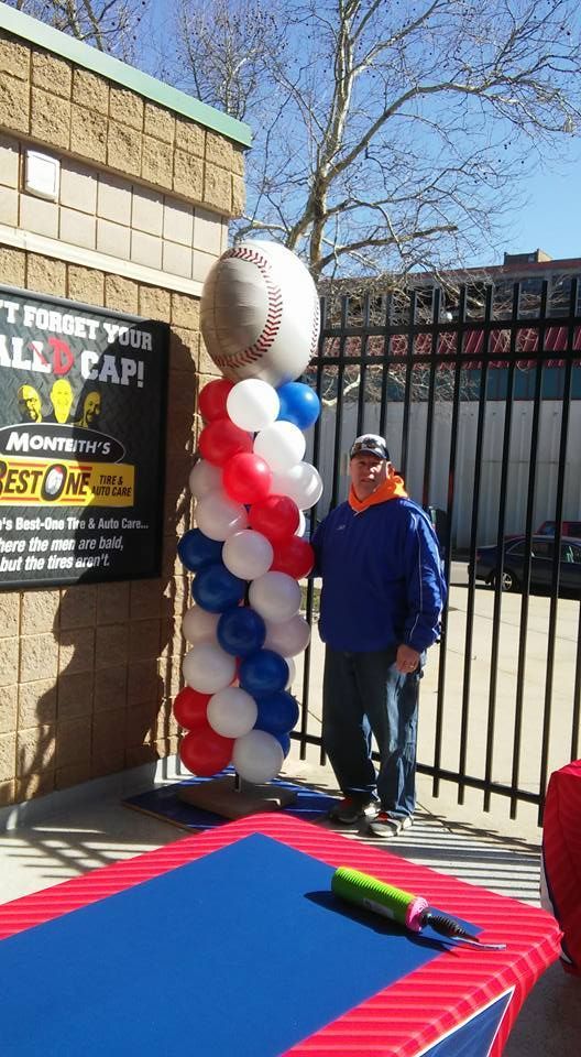 A man is standing next to a balloon column with a baseball on top of it.