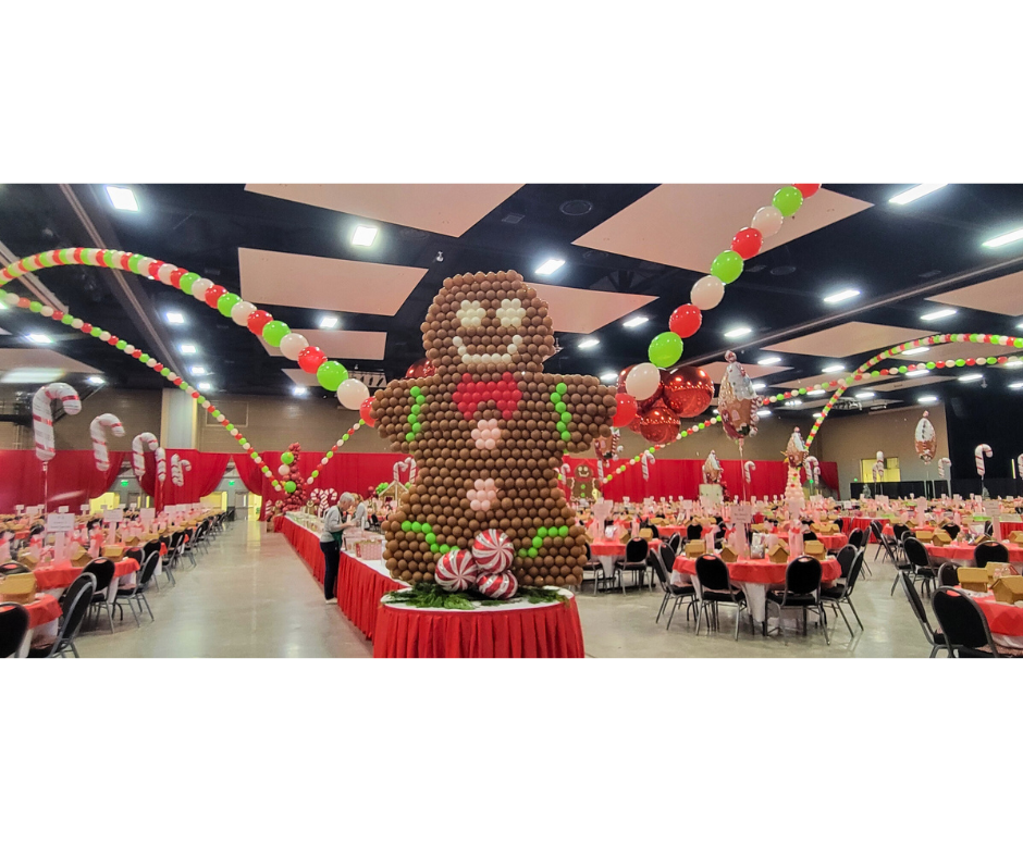 Gingerbread man balloon sculpture in decorated event hall, red and green decorations.