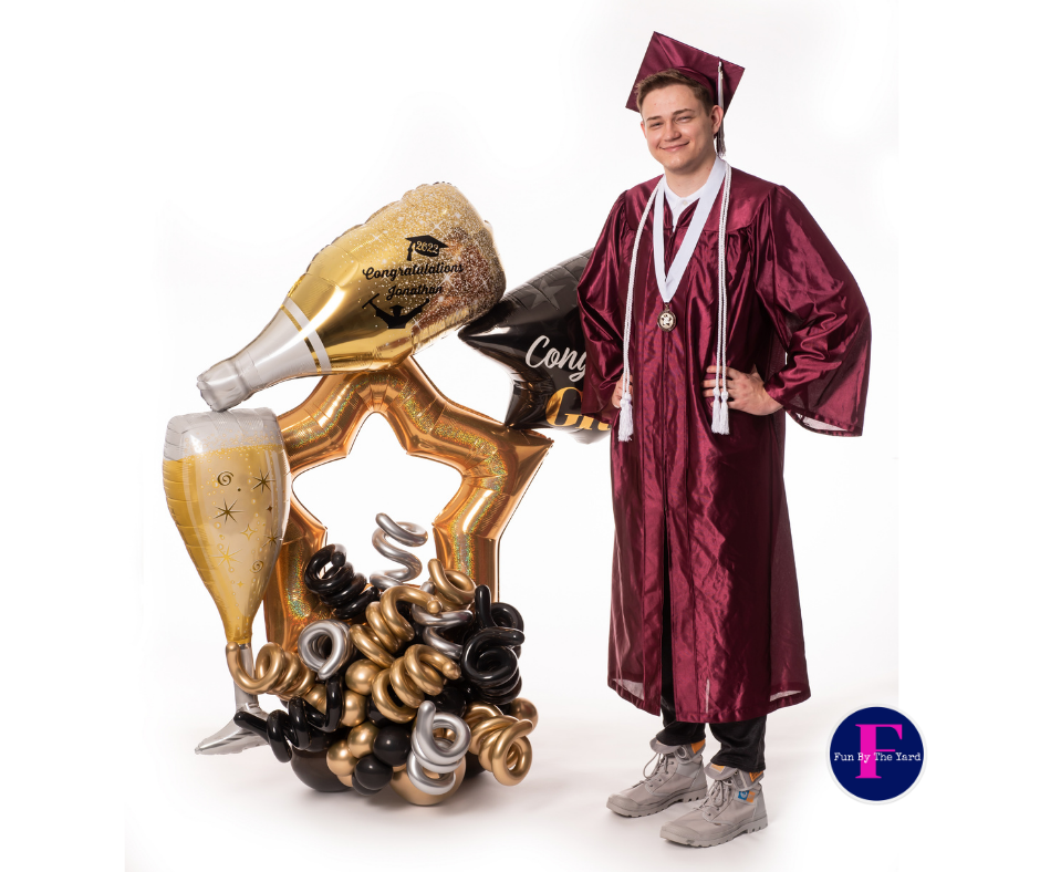 A man in a graduation cap and gown is standing next to a balloon arrangement.