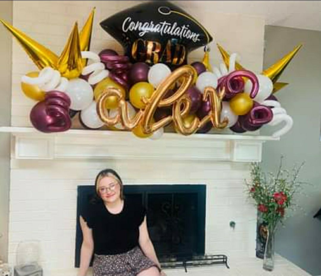A woman is sitting in front of a fireplace decorated with balloons and a graduation cap.