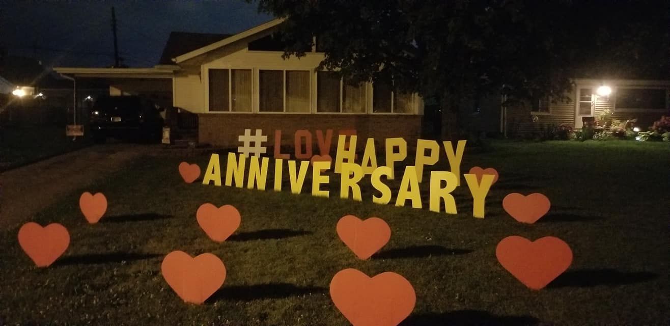 A sign that says happy anniversary with hearts in front of a house. Heart themed yard card.