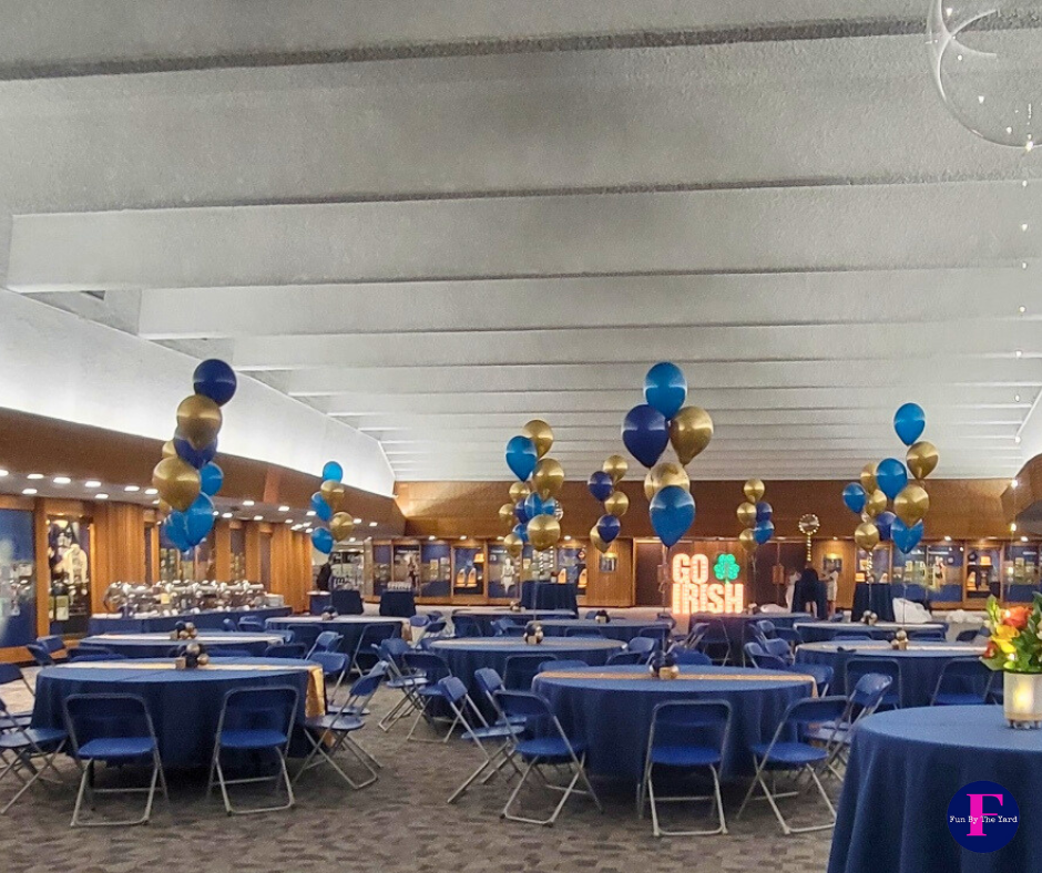 Event space with blue and gold balloon clusters, tables with blue tablecloths, and 
