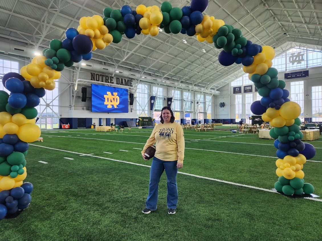 A woman is standing under a balloon arch on a football field at Notre Dame