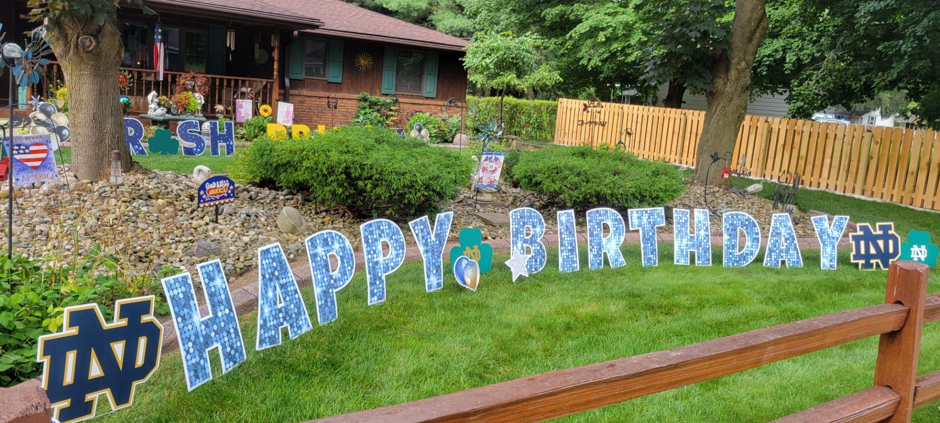 A wooden fence with a happy birthday sign in front of a house.