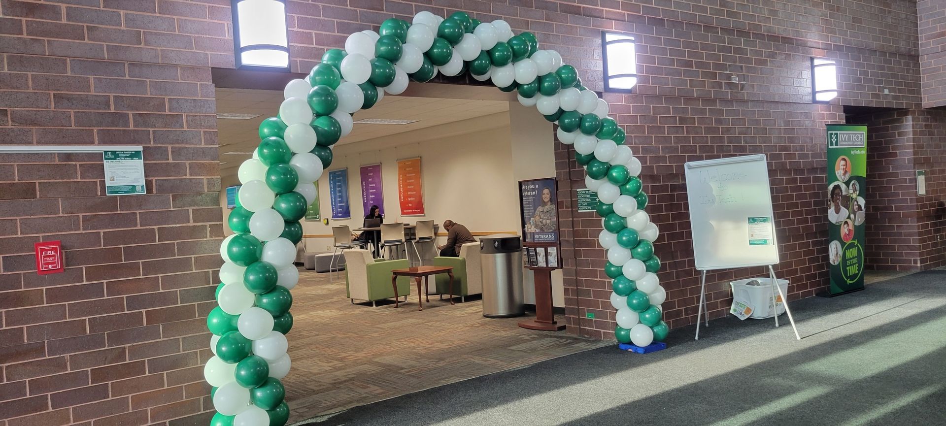 A green and white balloon arch is in front of a brick wall at Ivy Tech.