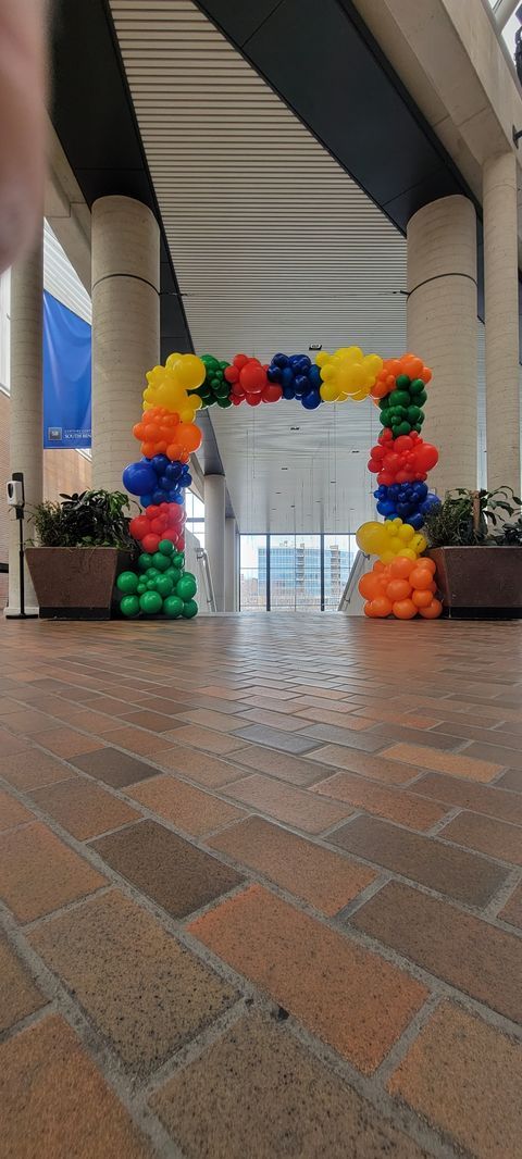 A person is standing in front of a balloon arch in a building.