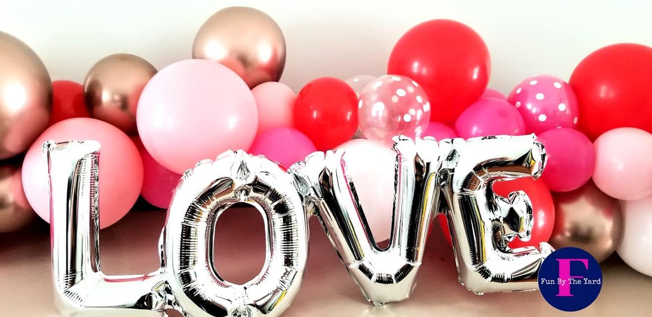 The word love is written in silver balloons surrounded by pink and red balloons.