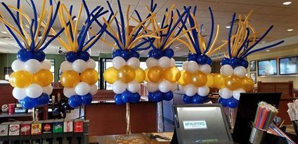 A restaurant is decorated with blue , white and gold balloons. Balloon party poles.