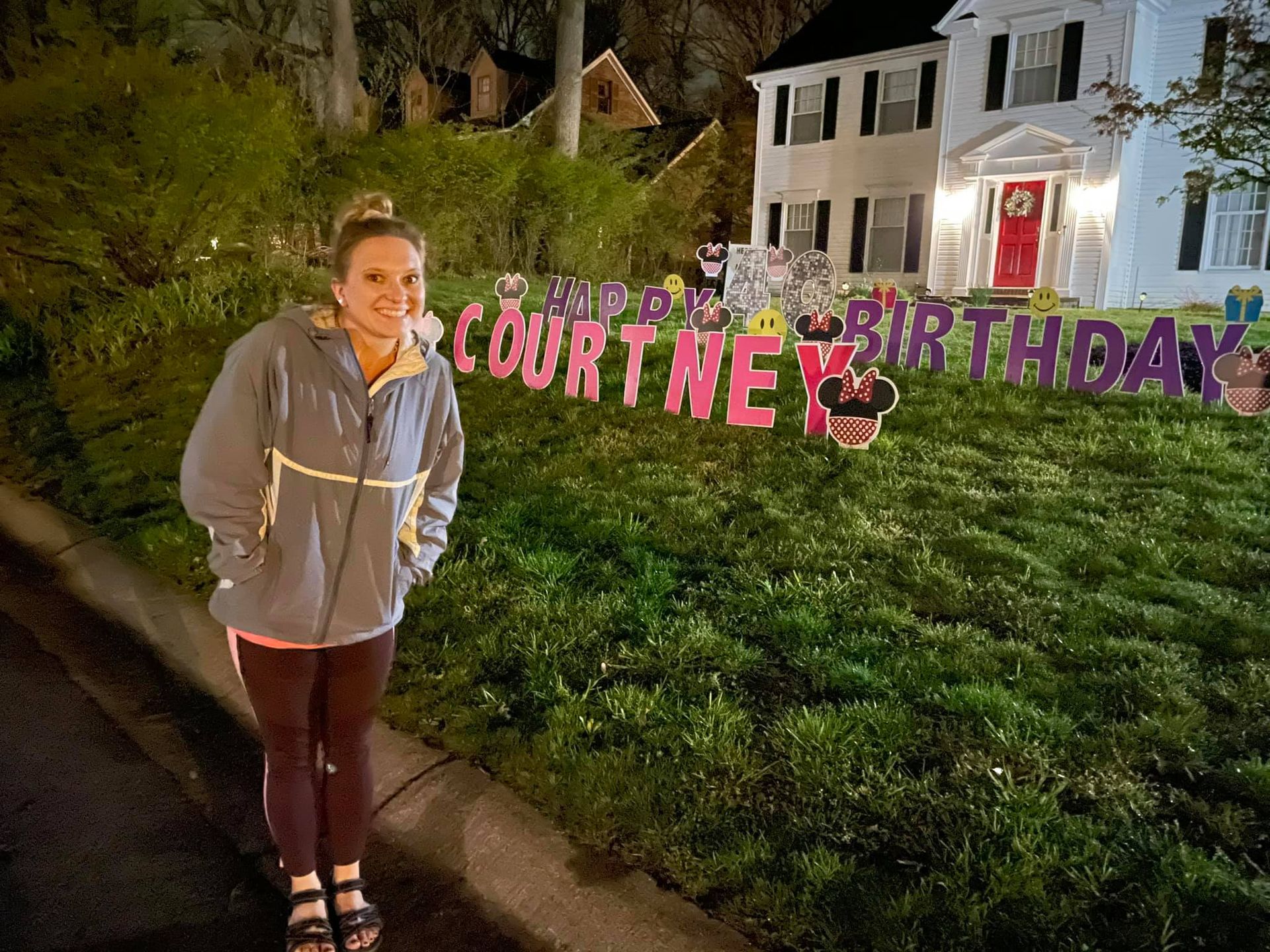 A woman is standing in front of a birthday sign in front of a house.