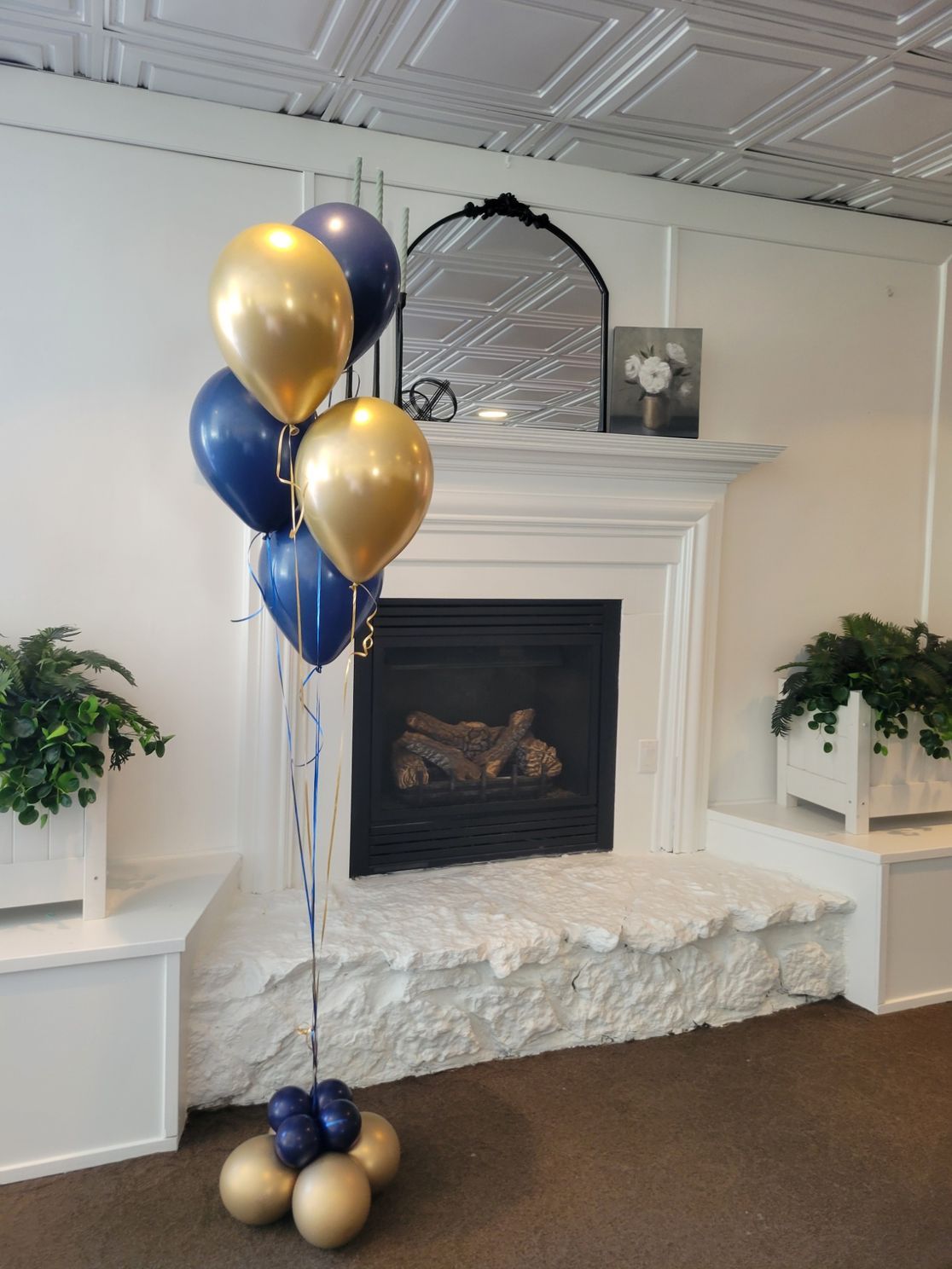 Balloon arrangement with gold and navy blue balloons in front of a fireplace.