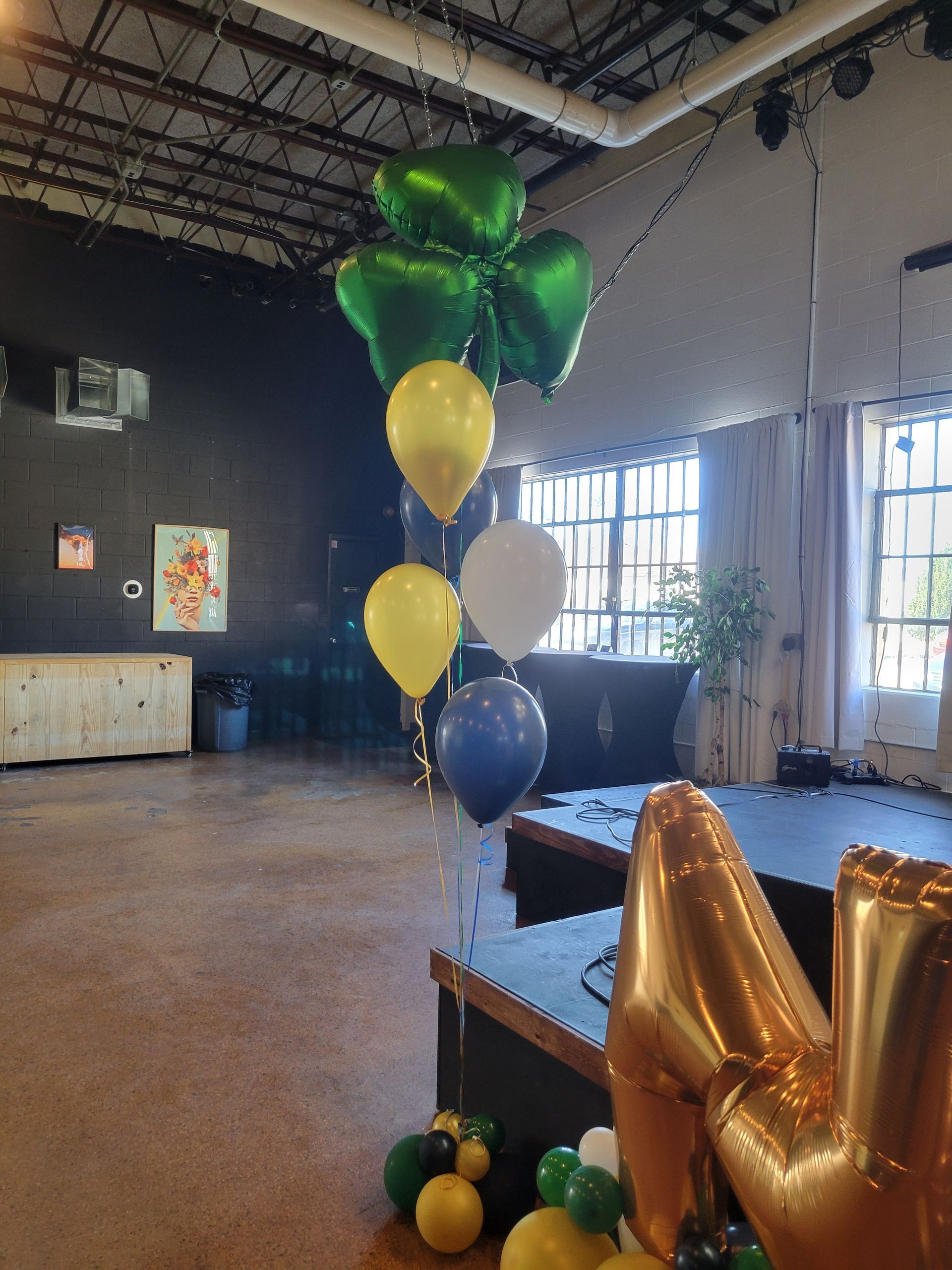 Balloons of green, yellow, white, and blue, including a clover shape, decorate a room, likely for a celebration.